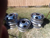 Stacked chrome trailer rims grouped with visible lug holes and circular ventilation holes, outdoors on grass.