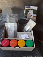 Full lot showing four colorful Teavana tea tins, unopened tea packages, dark brown glass pitcher, metal tea infuser spoon, and boxed Better Homes & Gardens wax warmer.