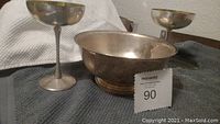 Photo showing two silver-tone wine goblets and a serving bowl on a grey cloth background