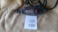 Photo of Dremel Moto-Tool Model 395 rotary tool laid on a beige surface with its power cord and a MaxSold auction tag numbered 146.