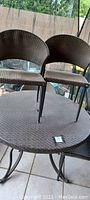 Two brown woven patio chairs placed on table surface showing woven pattern and curved backs.