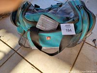 Photo of teal and black Swiss Gear duffle bag with a limited warranty card and auction tag visible