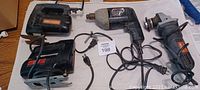 Four corded electric tools arranged on a surface: two jigsaws, one drill, one angle grinder.