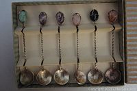 Full set of six handcrafted coin teaspoons with twisted handles and various semi-precious stones mounted at handle tops, displayed in box.