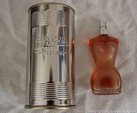 Jean Paul Gaultier Classique perfume torso bottle in amber color next to silver metal canister with embossed branding.