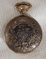 Front of watch showing embossed locomotive relief and floral scrollwork on gold plated case