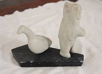Three-part Inuit carving including abstract woman and duck figures on a black base with visible chips.