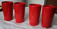 Four red Melmac tall cups aligned side-by-side on a white cloth.