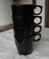 Four stacked black Melmac coffee cups with circular handles visible, showing height and shape.