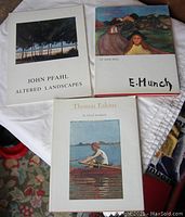 Three art books laid out on a white cloth: John Pfahl Altered Landscapes, E. Munch by Jean Selz, Thomas Eakins by Lloyd Goodrich.