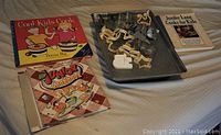 Photo showing 3 cookbooks 'Cool Kids Cook', 'Junior Cookbook', 'Jennifer Lagh Cooks for Kids', baking sheets with cookie cutters on top