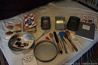 Overview of bakeware, cookbooks and baking tools neatly laid out on a bed for display.