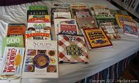 Full view of all cookbooks and home remedies laid fanned out on a bed showing all book covers and titles.