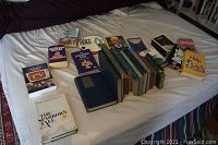 Overview of all books laid out on a bed, spanning various subjects and sizes, primarily hardcover with some paperbacks, in used condition.