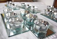 Six glass candle holders on rectangular mirrored bases, each with three silver-rimmed slots for floating candles.