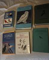 Six bird field guides placed on a fabric surface showing front covers and titles.