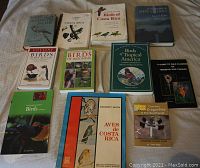 Photo showing 11 birding field guides laid out on a bed including titles about Costa Rica, South Pacific, New Guinea, Indonesia, Tropical America, New Zealand, Trinidad and Tobago wildflowers, and dragonflies of the Southwest.