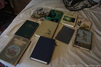 Full view of 11 birding books laid out on a bed, showing covers and bindings, including one titled 'Handbook of North American Birds Volume 1'