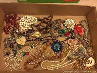 Box containing assorted vintage jewelry including multiple necklaces, beads, chains, and brooches in various colors and materials.
