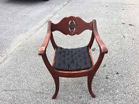 Front view of vintage wooden chair with black cushion showing curved armrests and ornate carved backrest.