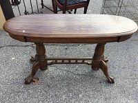 Full view of the wooden sofa table showing oval top, pedestal legs, claw feet, and stretcher base.
