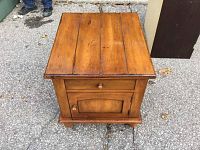 Front view of the small wooden washstand table showing the top surface, drawer, and door with round wooden knobs.