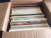 Top view of a large cardboard box filled with approximately 60 or more mixed vinyl LP records with varied album cover colors and designs.