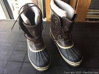 Pair of men's winter boots brown leather and black rubber shell, fleece lining visible, laced up.