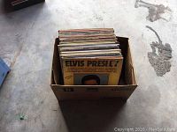 Cardboard box filled with approximately fifty vintage LP records. Top record is an Elvis Presley album.