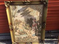 Full view of framed tapestry showing woman, sheep, bridge, and background cottage, with ornate gold-tone frame.