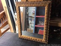 Full front view of the square beveled mirror in ornate gold-coloured decorative frame showing detailed relief pattern.
