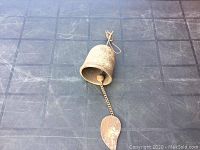 Full view of the cast iron bell lying on a black surface, showing bell, chain, and leaf-shaped end.
