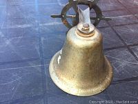 Front view of the nautical metal bell showing the bell and ship wheel mount on a dark surface.