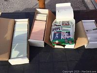 Photo showing several boxes filled with baseball cards, some cards loose and some stacked.