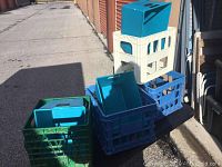 Photo showing five plastic milk crates in blue, cream, and green colors with multiple teal blue rectangular plastic storage containers with lids, arranged stacked on and inside the crates.