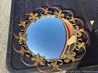 Overall view of the round decorative mirror with gold metal flower and vine frame.