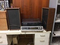 Full view of stereo unit with speakers on each side sitting on a metal desk. The stereo has a vintage aesthetic with wood and metal finishes.