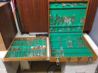 Open wooden case showing arrangement of flatware including forks, spoons, knives in green felt slots
