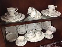Full view of upper and lower shelf display of china set showing matching plates, cups, saucers, bowls, creamer, and sugar bowl in Myott Blue Skies pattern.