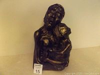 Front view of the bronze-colored sculpture depicting an Indigenous elder and child, showing emotional facial expressions and upper body details.