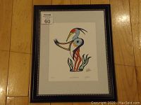 Photo of the framed fine art print showing the entire piece including the black frame with decorative trim and the stylized heron artwork inside.