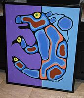 Front view of the full painting leaning against a stainless-steel range, showing purple left and blue right background, stylized bear figure, signature, and black wooden frame.