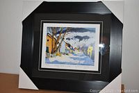 Front view of professionally framed and matted print showing winter village street scene by Clarence Gagnon, including protective corner guards on frame.