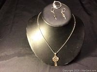 Jewelry set displayed on a black stand with necklace pendant, earrings, and brooch visible.