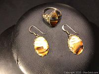 Ring and matching earrings displayed on black surface showing the oval brown and golden tiger's eye-style stones and silver setting.