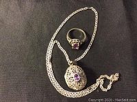 Necklace chain with locket pendant and ring displayed side by side on black background