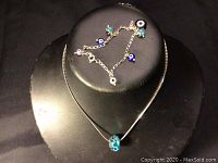 Sterling silver necklace displayed on a black bust with a blue glass bead pendant and a sterling silver charm bracelet with colorful charms.
