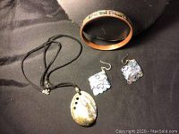 Full jewelry set on black cloth background including mother of pearl pendant necklace, sterling silver hook earrings with mother of pearl, and pinkish-orange bangle with Inukshuk and mother of pearl detail.