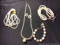 Image showing three pearl bracelets, one with a toggle clasp and one multistrand bracelet, a pearl necklace with flower accents, and one pearl bracelet with larger beads and extender clasp.