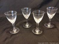 Four Baccarat crystal liquor glasses arranged with space in between on a black background.
